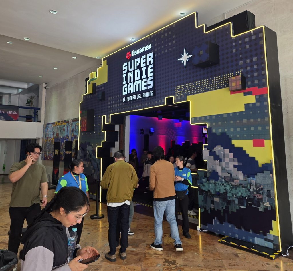 Entrance to the Super Indie Games event, featuring a large, colorful display with the text 'Banamex SUPER INDIE GAMES El Futuro del Gaming,' surrounded by attendees mingling and interacting.
