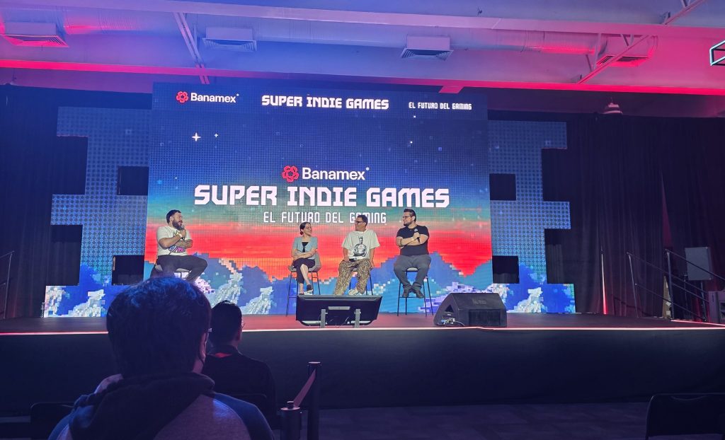 A panel discussion at the Super Indie Games event, featuring four speakers on stage with a colorful backdrop displaying the event name and theme related to the future of gaming.