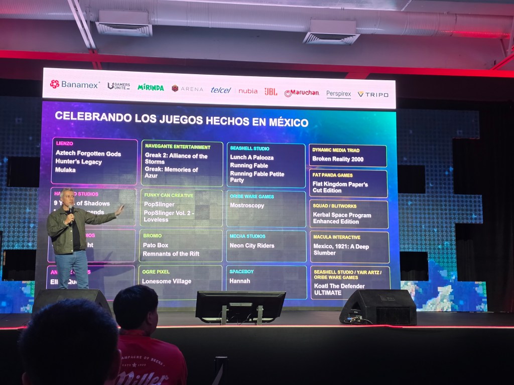 A speaker presenting at an event titled 'Celebrating Games Made in Mexico,' showcasing various video games and their developers, with a colorful digital backdrop and audience in view.