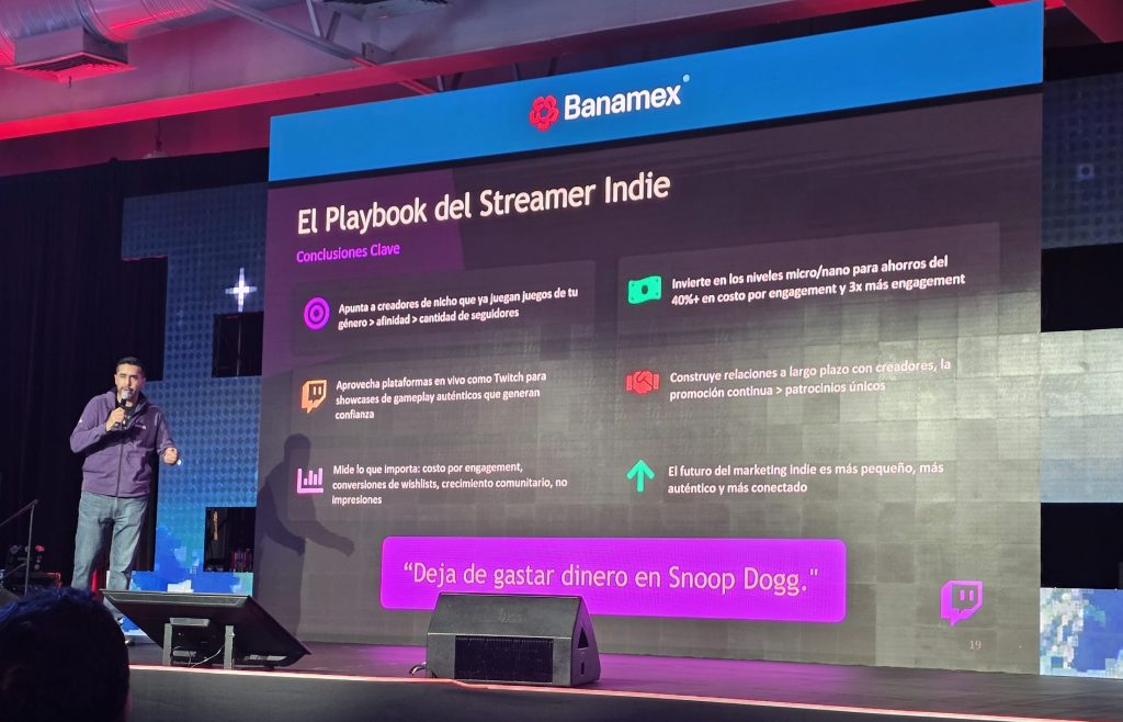 A speaker presents insights on indie streaming at a conference, with a slide titled 'El Playbook del Streamer Indie' displaying key conclusions. The background features a stage setup with lighting and a screen showcasing bullet points about engaging niche creators and utilizing platforms like Twitch.